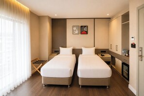 Ein Hotelzimmer mit zwei Betten, einem Kleiderschrank, einem Nachttisch mit Telefon und einem Fenster mit Vorhängen.