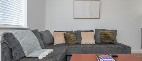 Una sala de estar moderna con un sofá seccional gris, una mesa de centro de madera y una obra de arte abstracta enmarcada en la pared.