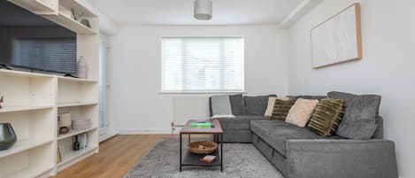 Un salon moderne avec un canapé gris, une petite table et une bibliothèque.