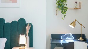 Ett modernt sovrum med en turkos sänggavel, en sänglampa och en neonskylt.