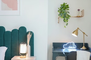 Ein modernes Schlafzimmer mit einem petrolfarbenen Kopfteil, einer Nachttischlampe und einem Neonzeichen.