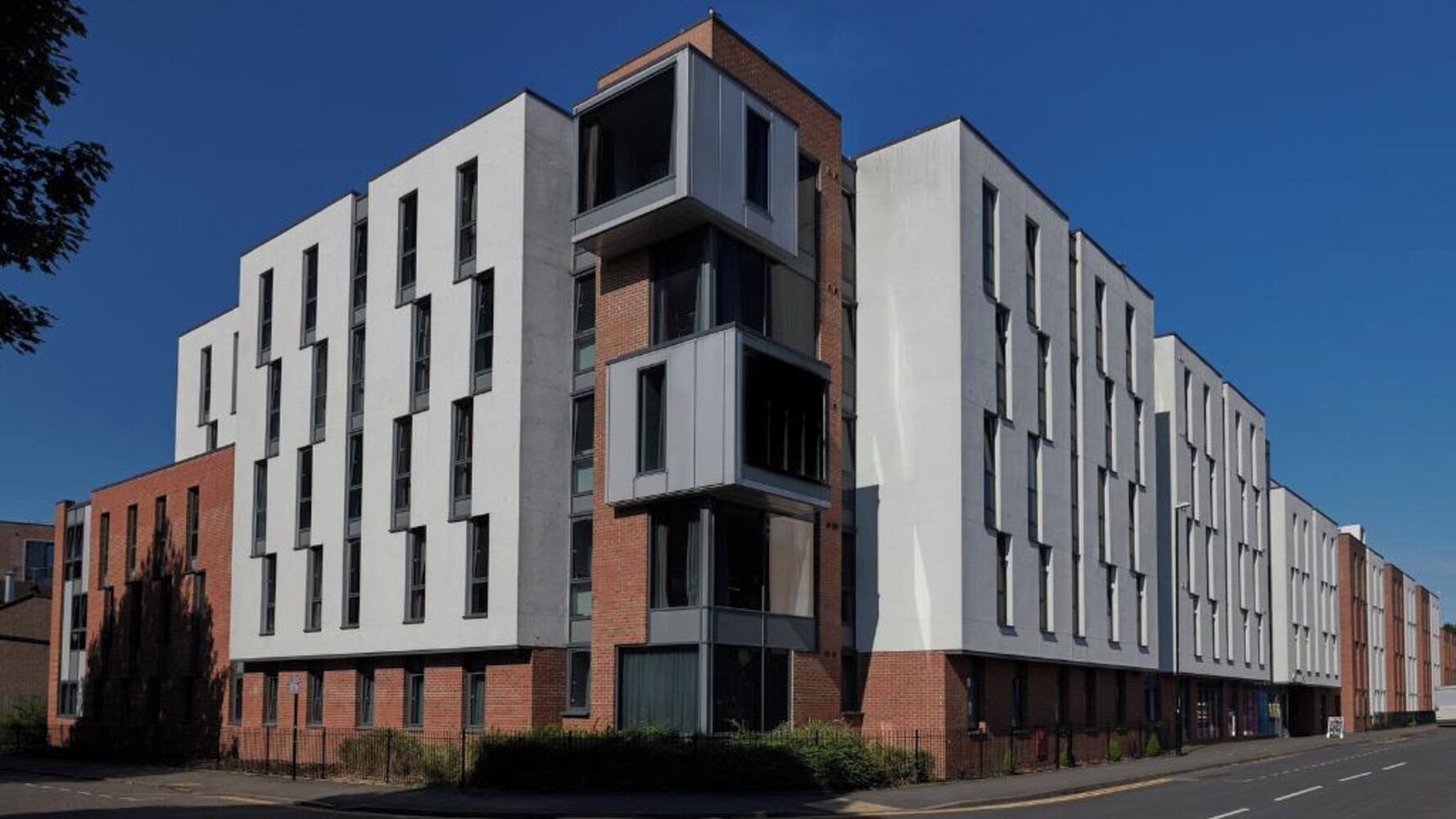 Een meerhoog gebouw met een modern architectonisch ontwerp, dat baksteen en witte gevels combineert, en een reeks ramen op elke verdieping heeft.