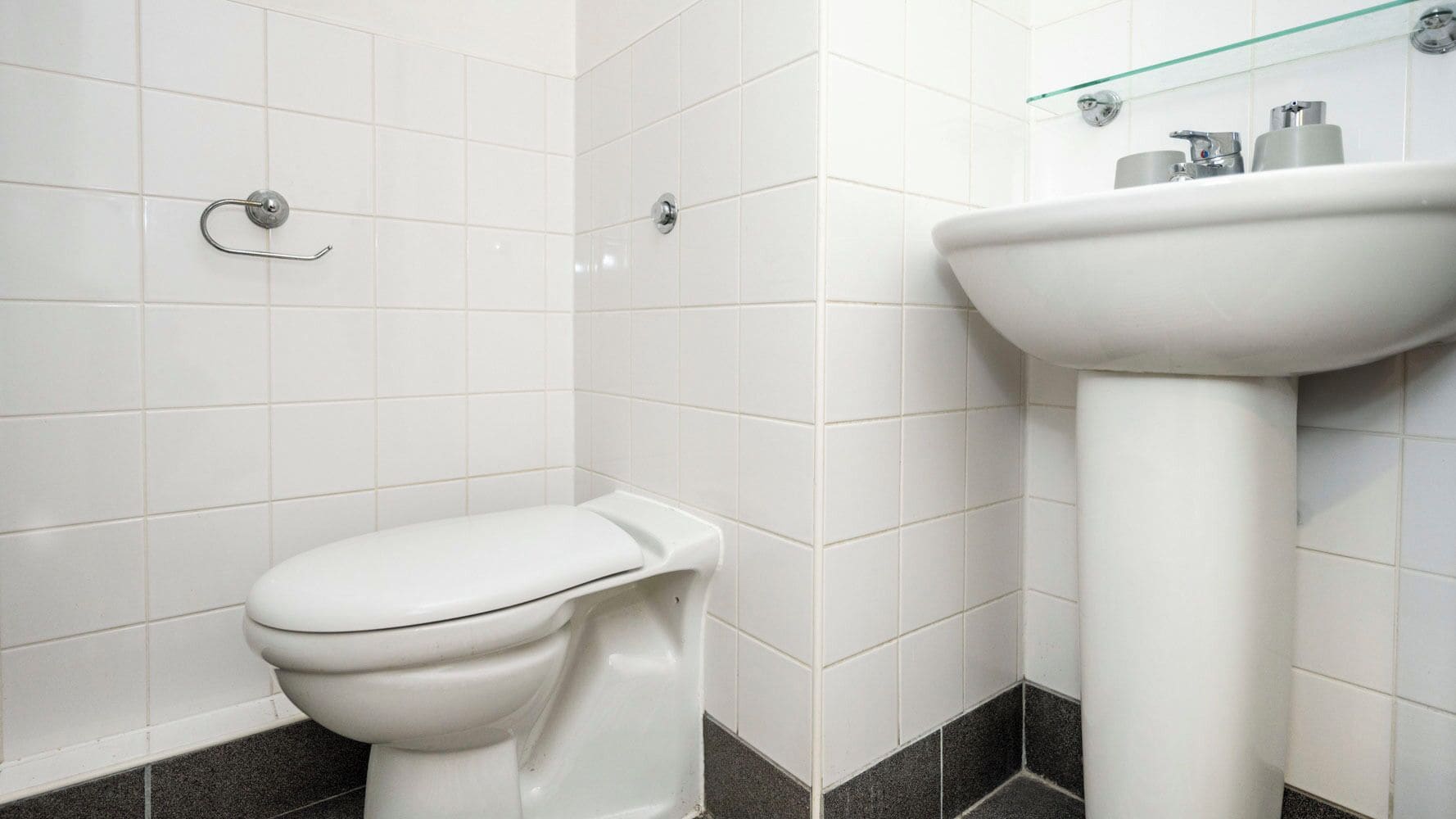Un baño con inodoro blanco y lavamanos sobre pedestal.