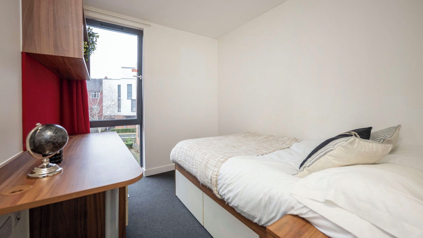 A bedroom with a bed, a desk, and a window.