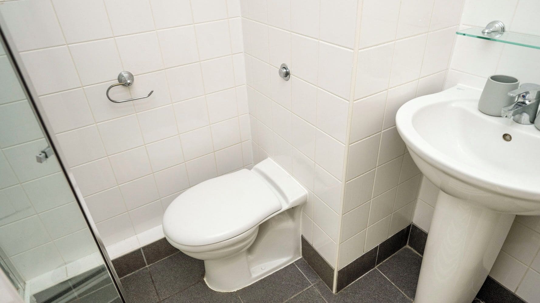Et lille badeværelse med toilet, vask og en glashylde.