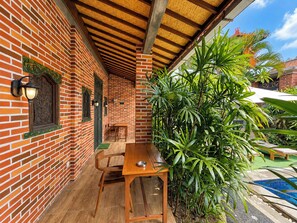Un bâtiment en briques avec une table et des chaises en bois, une petite piscine et une végétation luxuriante.