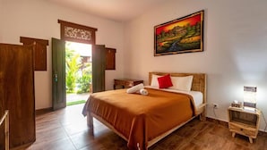 A hotel room with a bed, a nightstand, a painting, and a view of greenery outside.
