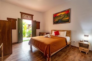 A hotel room with a bed, a nightstand, a painting, and a view of greenery outside.
