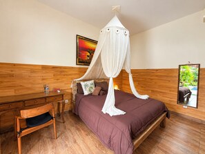 A bedroom with a four-poster canopy bed, a wooden headboard, a desk with a chair, and a painting on the wall. - Pondok Juli Canggu (Canggu)