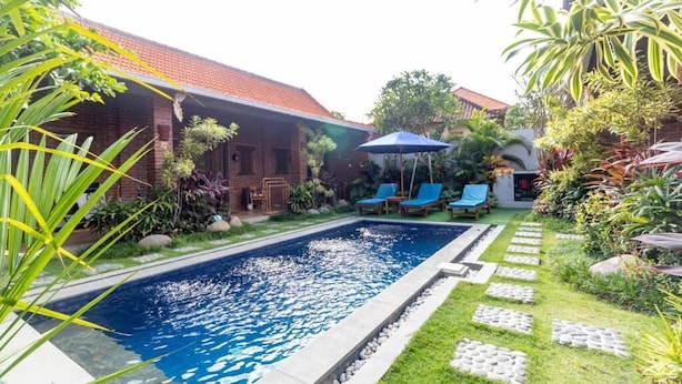 A swimming pool with a surrounding garden, a brick building, and lounge chairs.