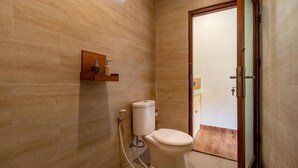 A compact bathroom with a toilet, a wooden shelf, and a door leading to another room.