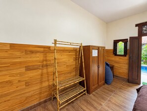 Een kamer met een houten wand, een bamboe plank, een kledingkast en een deur naar een buitenruimte.