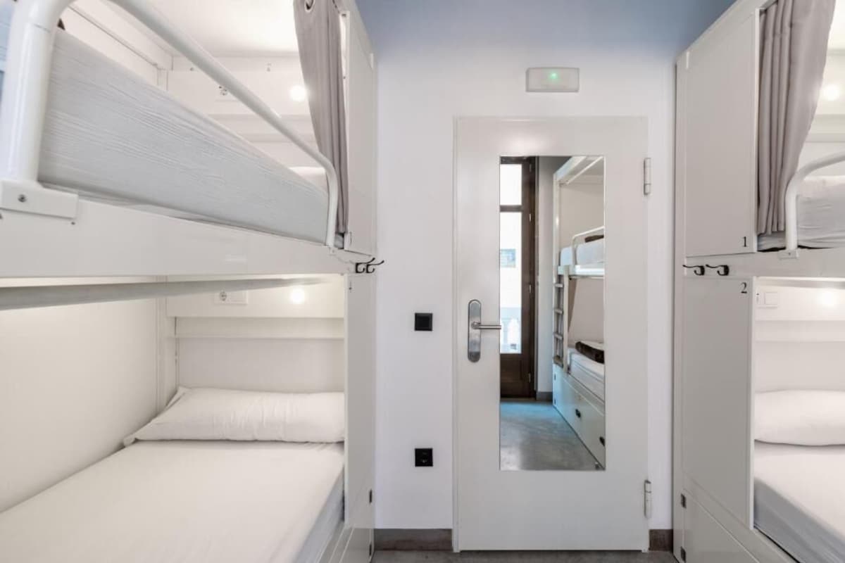 A narrow corridor with bunk beds on either side, a door at the end, and a mirror reflecting the corridor.