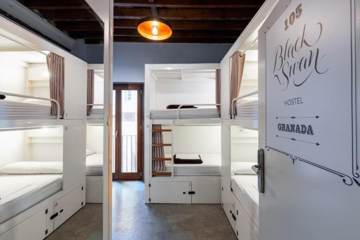 A bunk bed room with a sign indicating it is the 105 Black Swan Hostel in Granada.