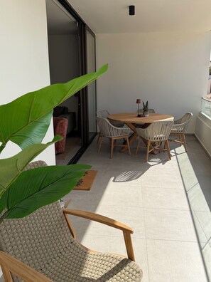 A modern outdoor dining area with a round table and wicker chairs, a potted plant, and a sliding glass door leading to an interior space. - New! Luxury 2-bedroom apartment with shared pool, only 5 minutes to Mambo Beach (Unknown)
