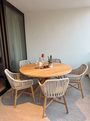 Une table ronde en bois, entourée de quatre chaises en osier, avec une plante en pot et une bouteille de vin posées sur la table.