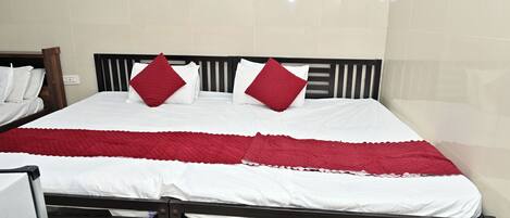 Una cama con una colcha blanca y roja, dos almohadas rojas y un cabecero de madera.