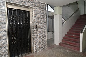 A staircase with red steps leading to an upper floor, a metal gate with a digital display, and a stone wall with a textured pattern.