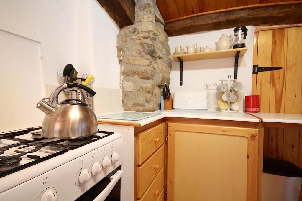 Una cocina con estufa a gas, armarios de madera, pared de piedra y repisas con utensilios de cocina.