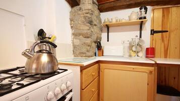 Una cocina con estufa a gas, armarios de madera, pared de piedra y repisas con utensilios de cocina.