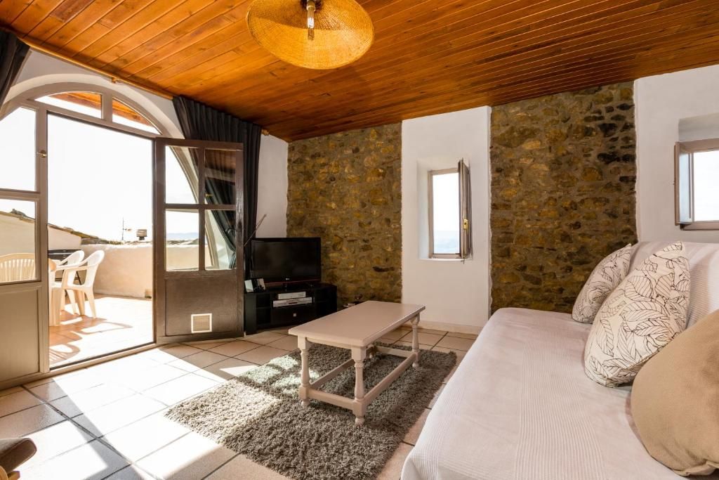 Un salon chaleureux avec un mur en pierre, un canapé, un téléviseur et un coin repas avec des chaises.