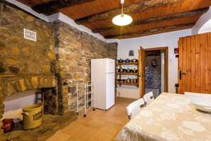 A rustic kitchen with stone walls, a white refrigerator, and a wooden ceiling. - Casa Mauri (Santa Engràcia)