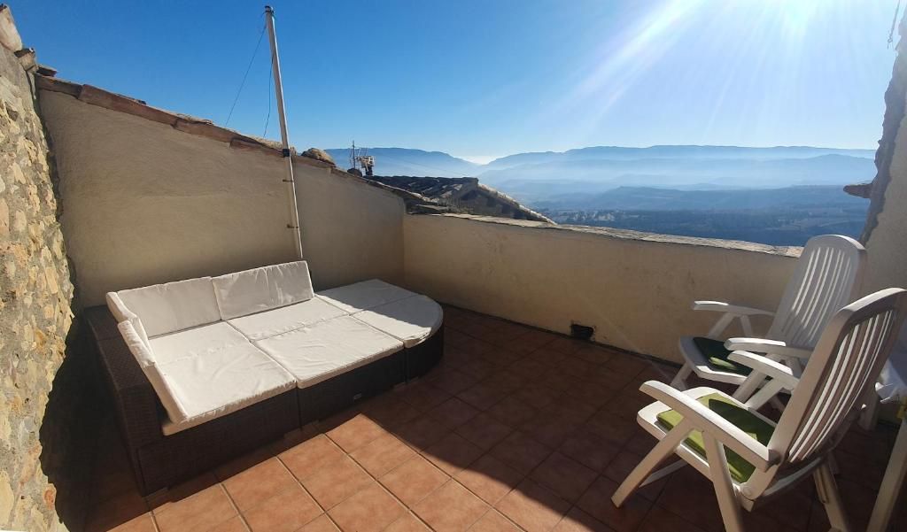 Un balcón con un sofá, sillas y vistas a montañas distantes.
