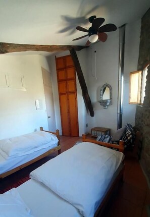 A room with two single beds, a ceiling fan, a wooden door, and a window. - Casa Mauri (Santa Engràcia)