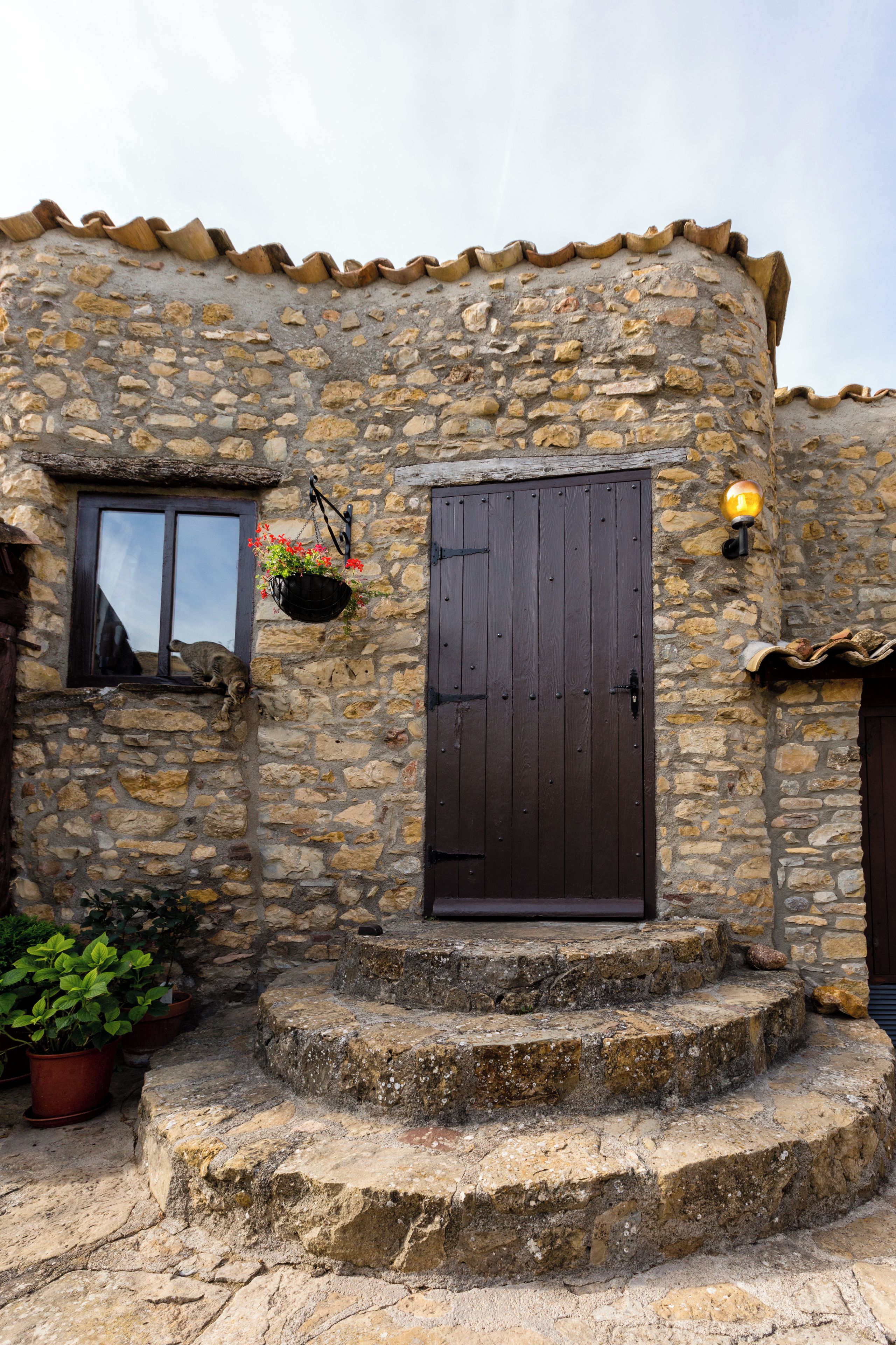 Edifici de pedra amb una porta de fusta, una finestra amb una cistella de flors penjant i una petita escala que condueix a l'entrada.