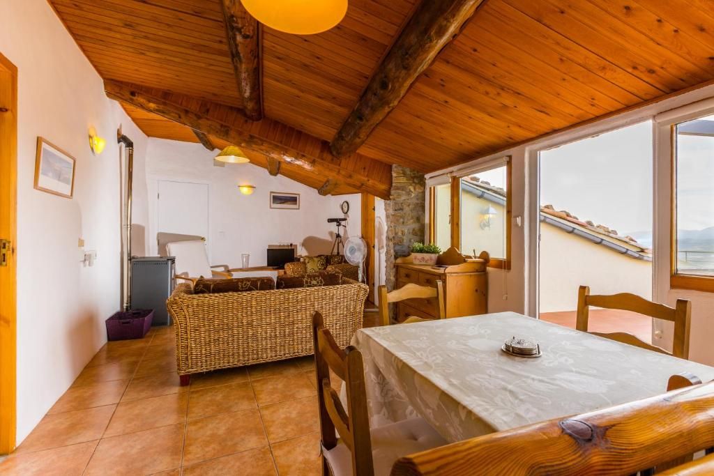 Una habitación acogedora con techo de madera, una mesa de comedor, muebles de mimbre y vistas a través de un ventanal.
