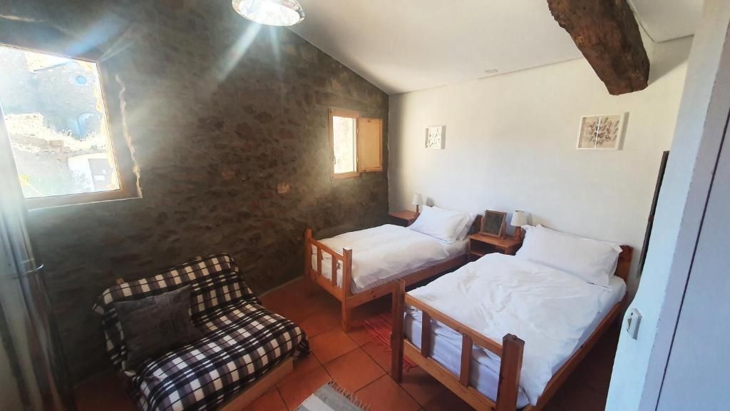 Una habitación con dos camas de madera, un sofá a cuadros y un ventanal.