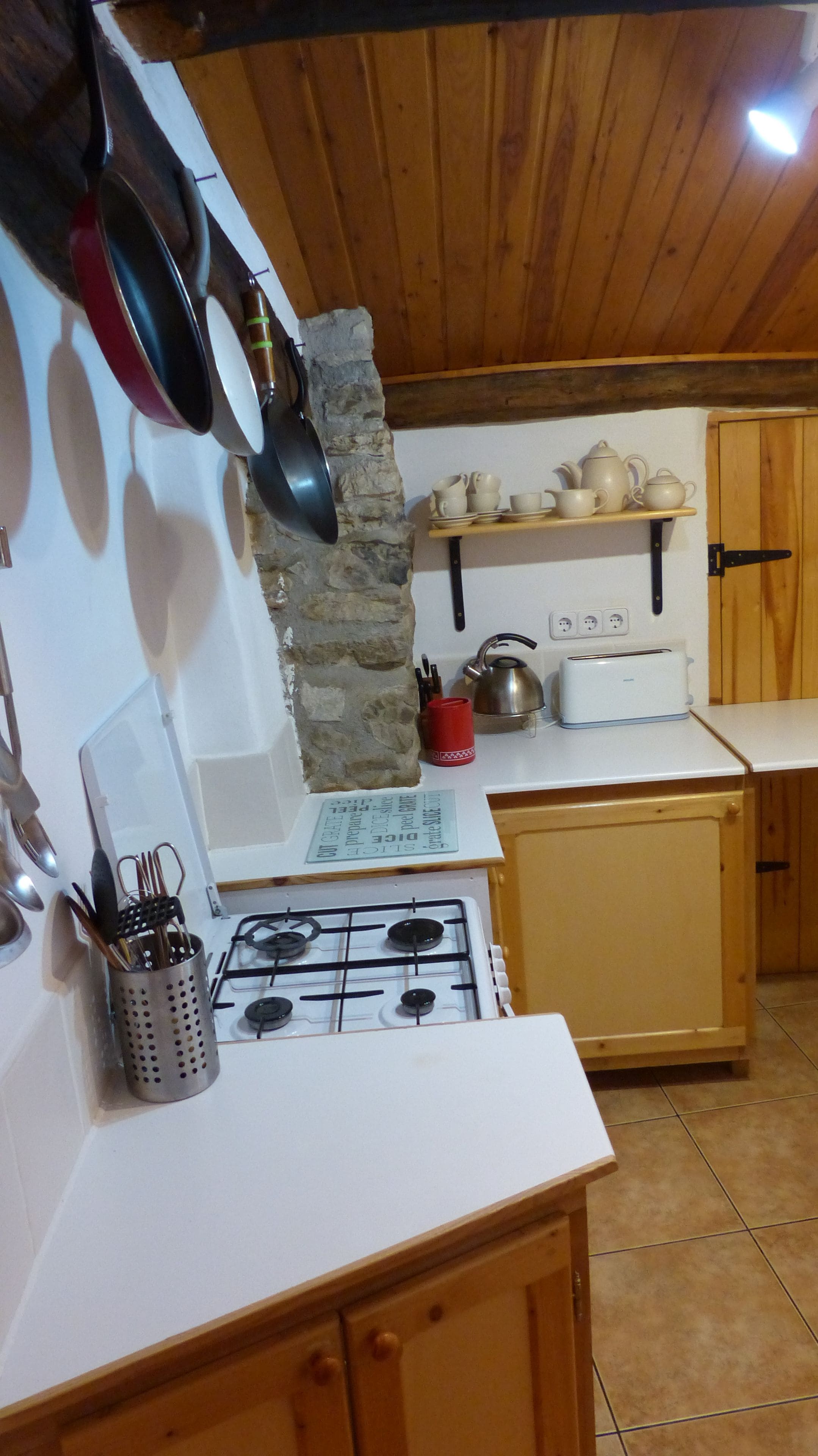 A kitchen with a gas stove, wooden cabinets, a stone wall, and various kitchen utensils.