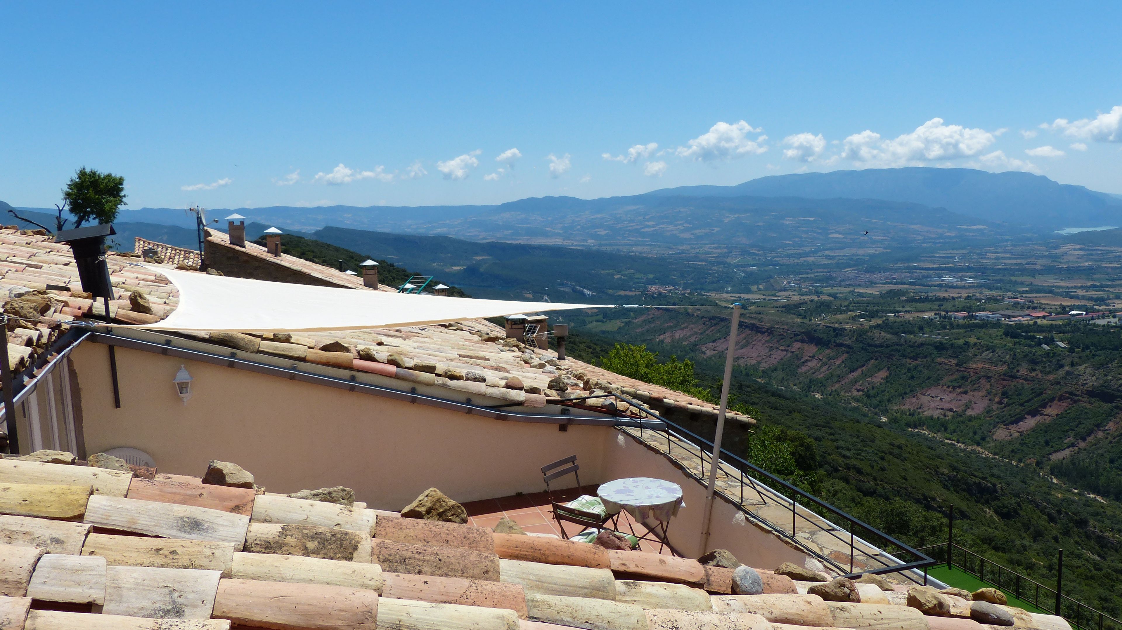 Una terraza con vistas a un valle y montañas, muros de piedra y una mesa con sillas.