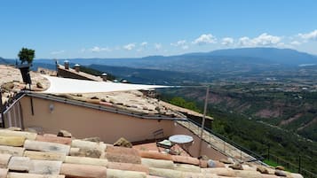 Una terraza con vistas a un valle y montañas, muros de piedra y una mesa con sillas.