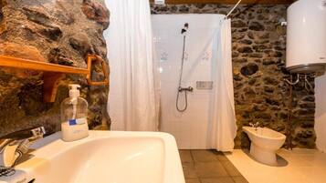Une salle de bain avec un mur en pierre, un lavabo, une douche et un bidet.