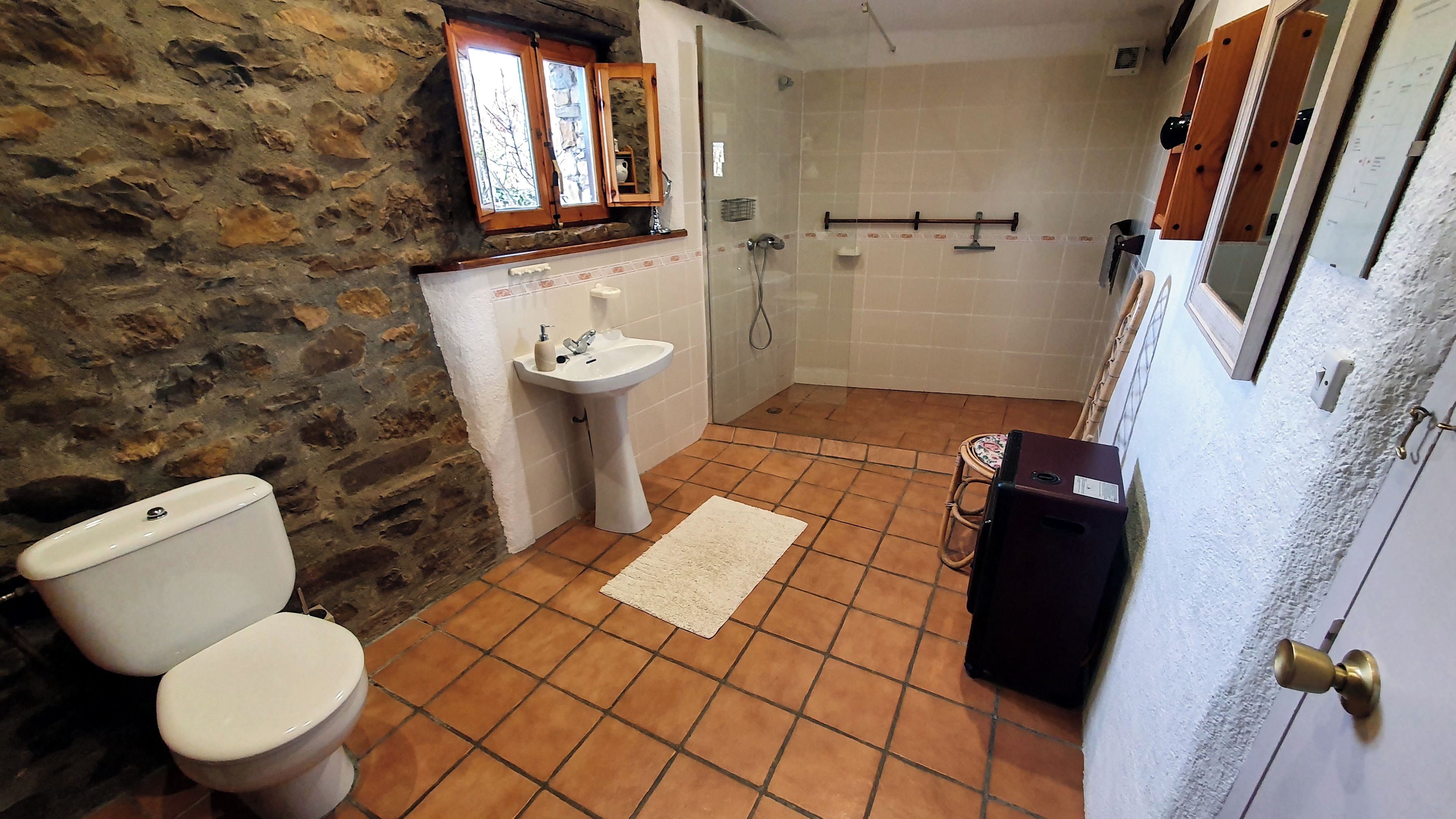 A bathroom with a stone wall, a toilet, a sink, and a shower.