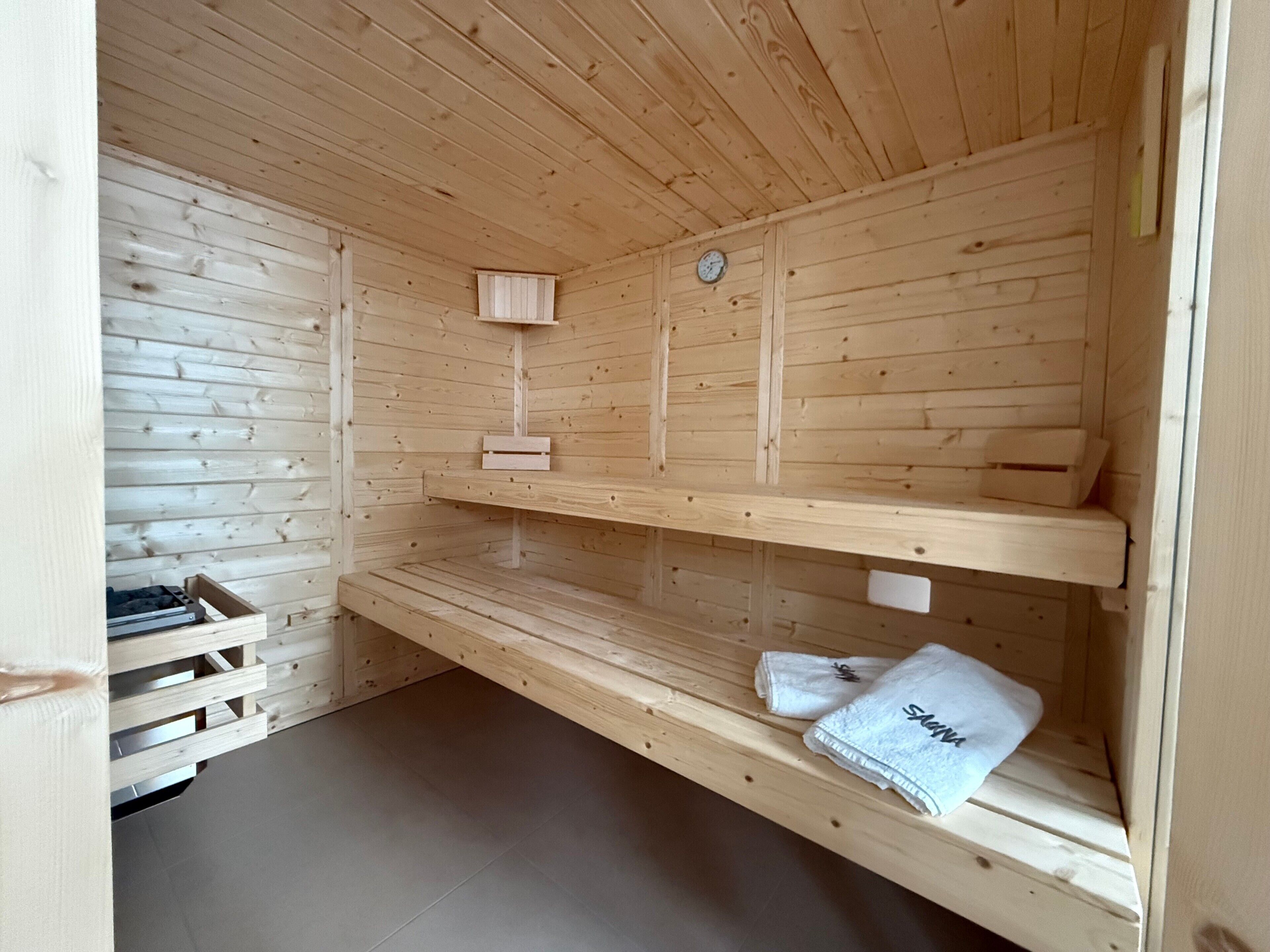 A sauna room with wooden walls and benches, a clock, and a towel on one of the benches.