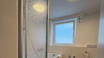 Ein Badezimmer mit Duschkabine aus Glas, einer Badewanne, einem Fenster und einem Handtuchhalter.