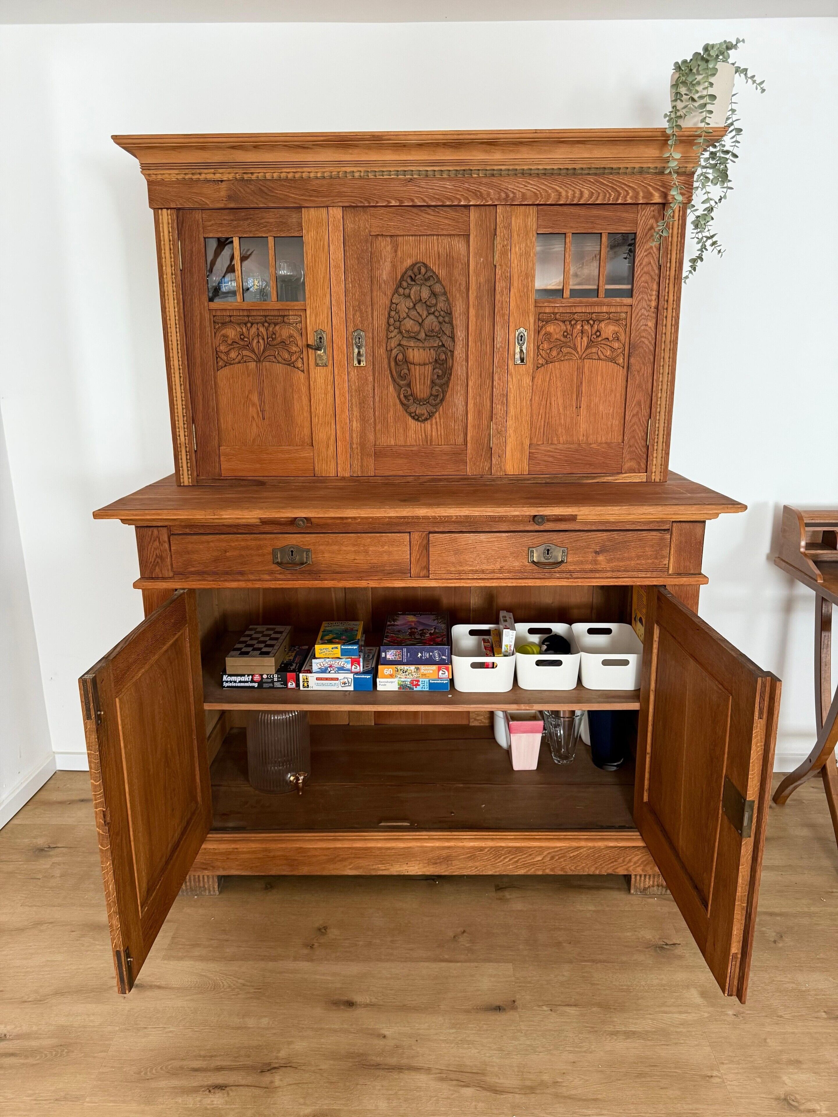 Ein Holzkabinent mit mehreren Fächern, darunter Schubladen und Regalen, in denen sich beispielsweise Brettspiele und Aufbewahrungsboxen befinden.