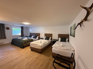 Habitación de hotel con dos camas, una mesita, una ventana con cortinas y una obra de arte en la pared.