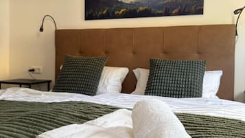 Een netjes opgemaakt bed met een groen gebreid plaid en twee witte handdoeken, een bruin hoofdbord en een schilderij van een zonsondergang aan de muur.