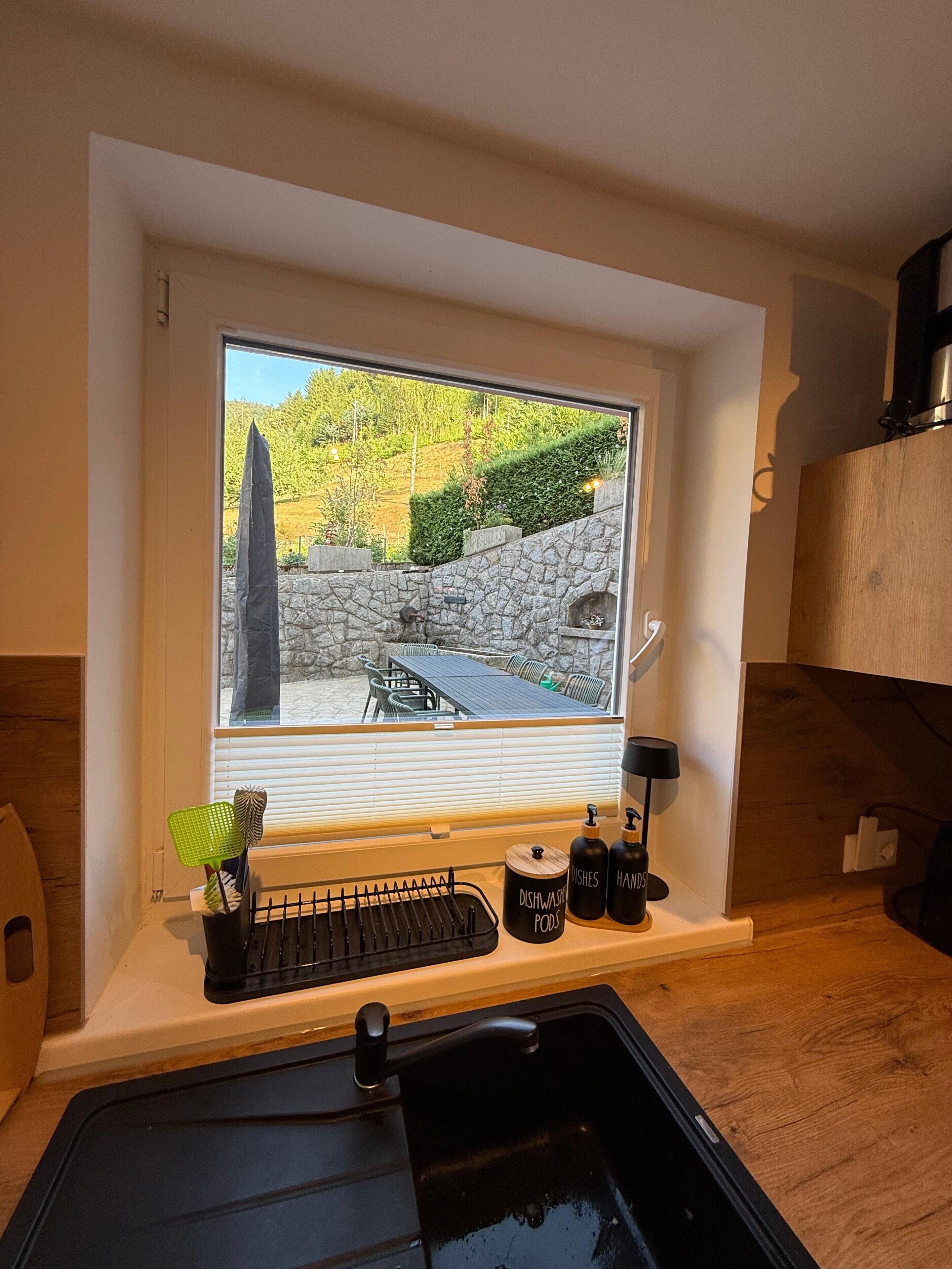 Eine Küche mit integriertem Fenster, das auf eine Steinmauer und eine Außenlounge blickt.