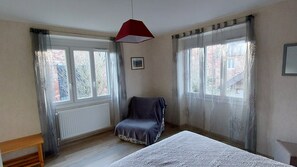 Ein Zimmer mit Bett, einem Sessel und einem fenster mit Vorhängen.