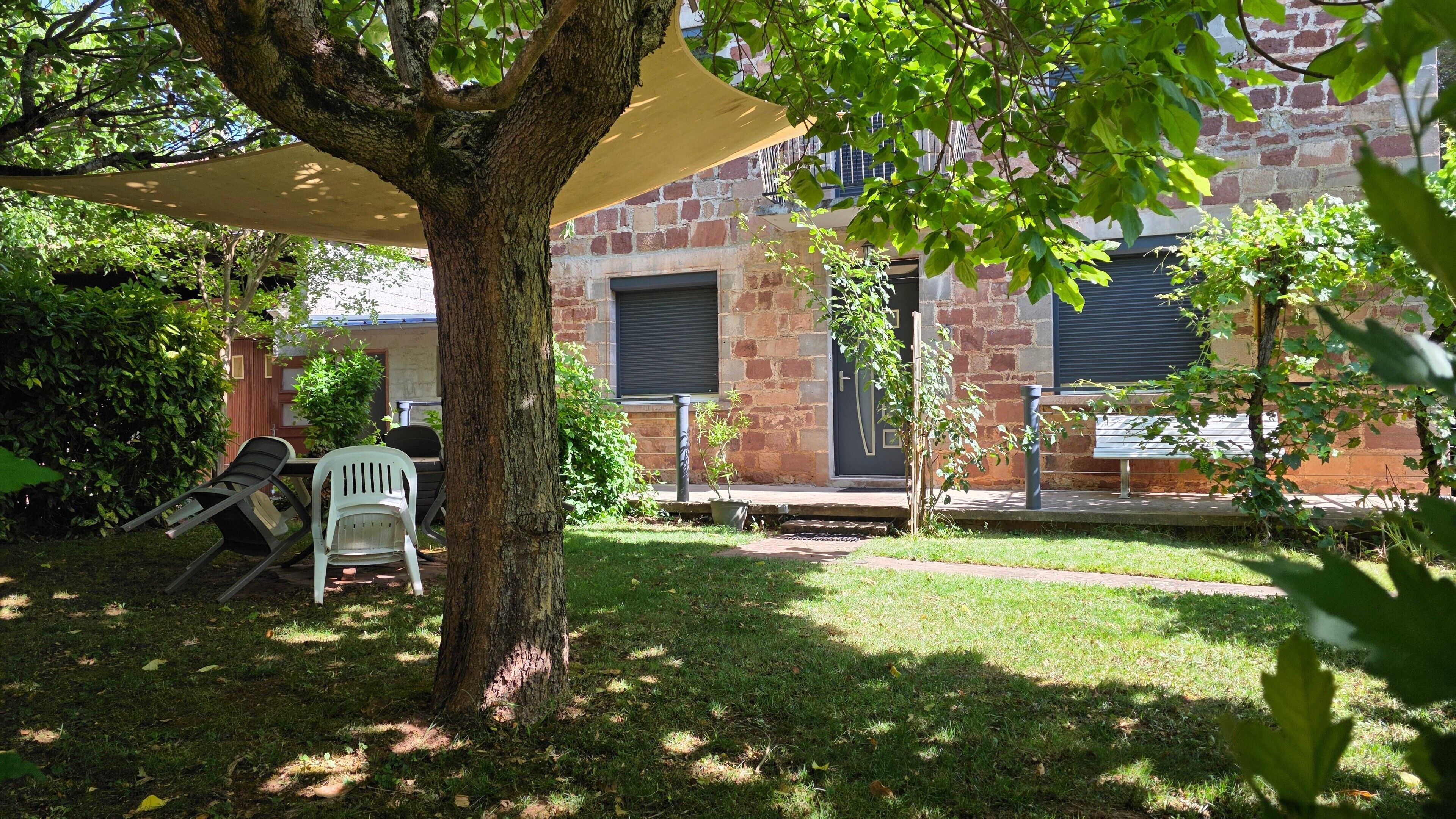 A courtyard with a tree, a white plastic chair, a potted plant, and a brick building with a window and door.