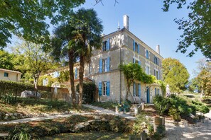 A stone building with blue shutters, surrounded by trees and a gravel path.
