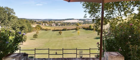 A patio with a table and chairs, overlooking a rural landscape with fields and trees.