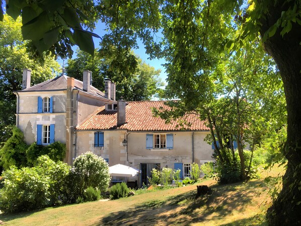 A two-story house with a tiled roof, surrounded by greenery and trees.