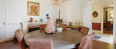 Uma sala de jantar com uma mesa redonda, cadeiras, lareira e um quadro na parede.