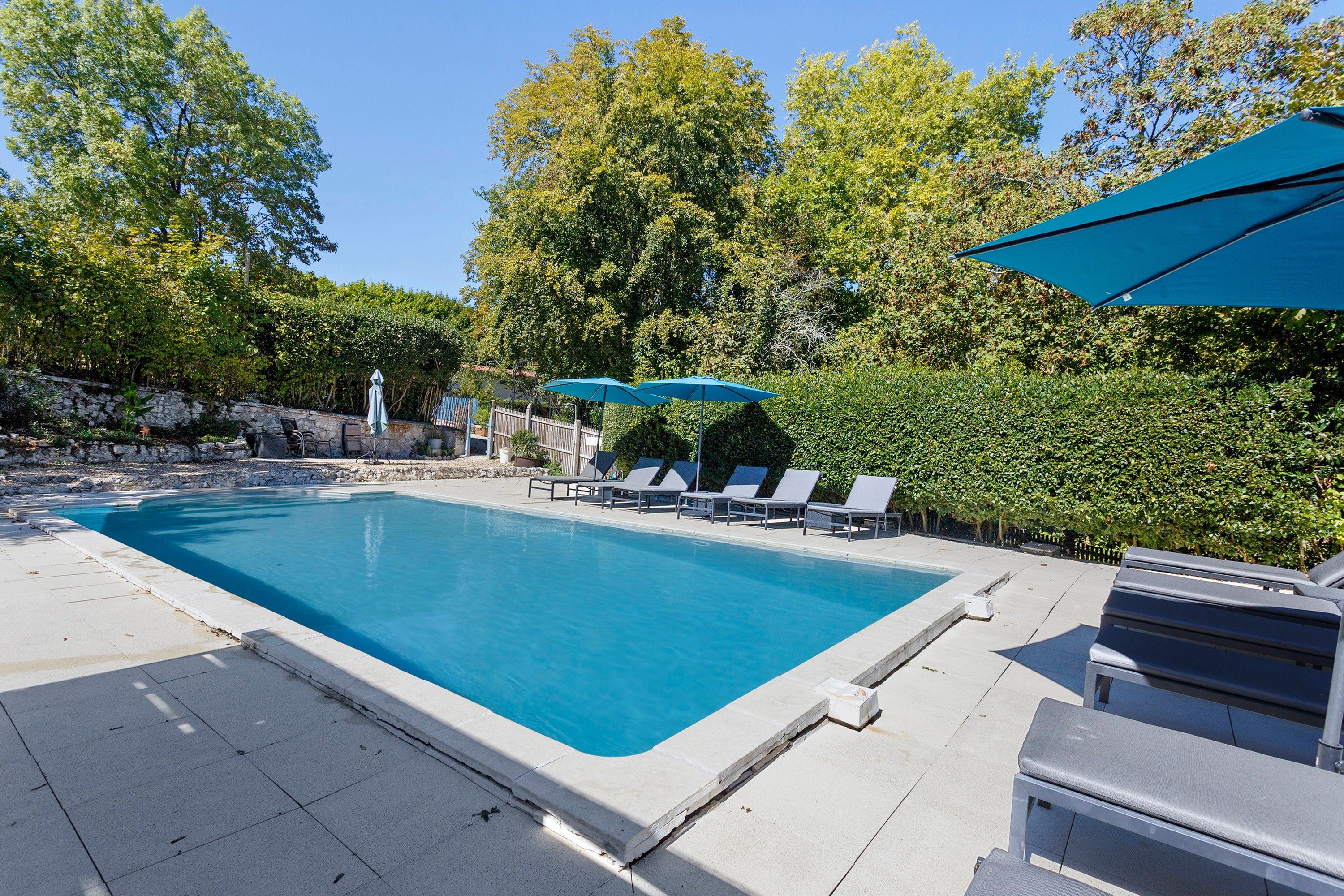 Une piscine rectangulaire bordée de pierres, entourée de chaises longues et de parasols.