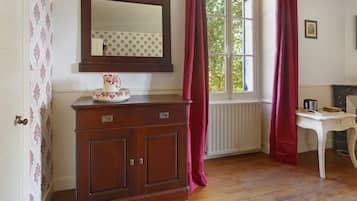 A room with a wooden cabinet, a mirror, a window with curtains, a radiator, and a small table with a kettle.